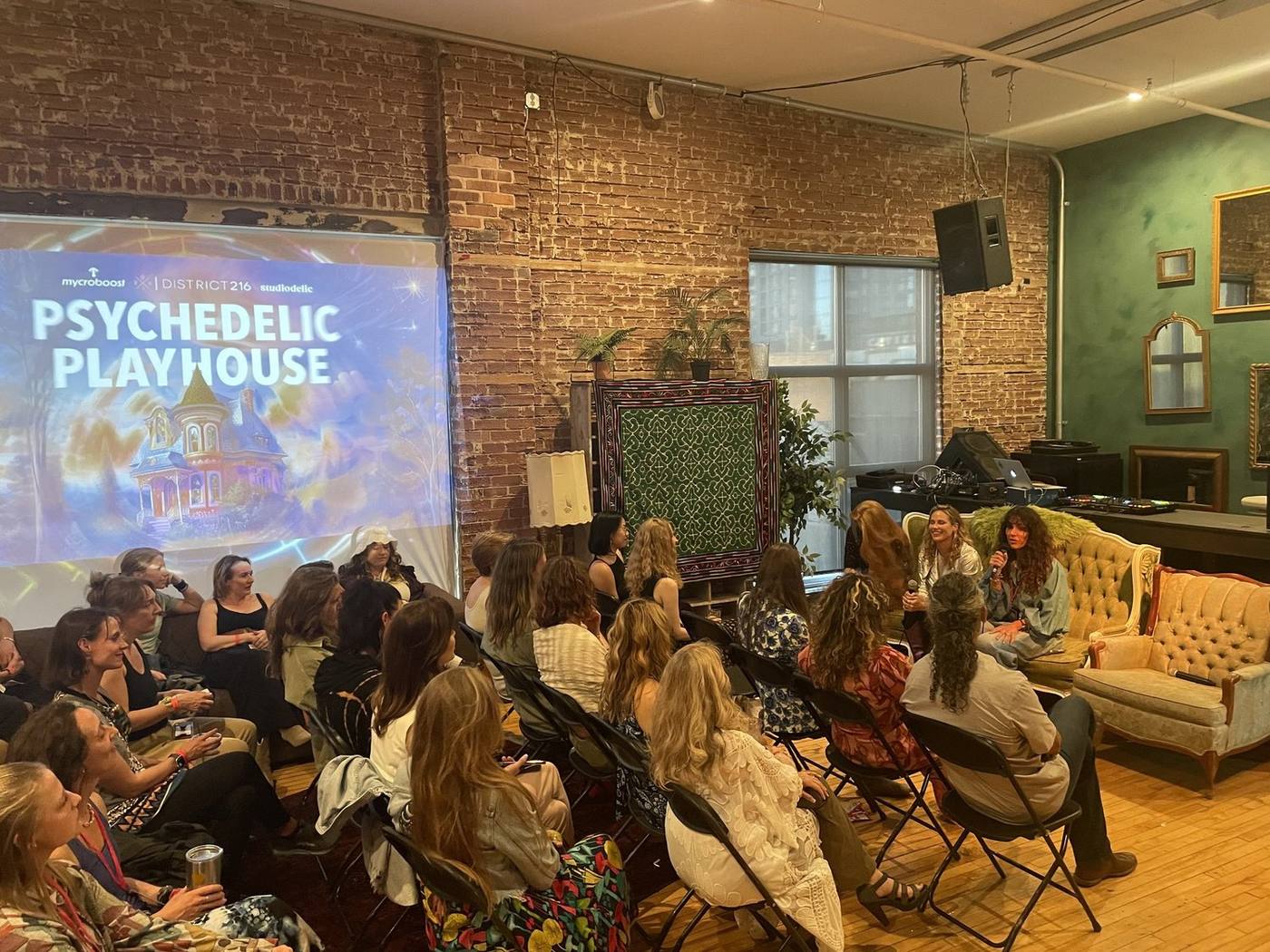 A packed salon room with guests on vintage sofas facing a projected Psychedelic Playhouse title slide.
